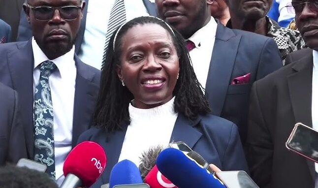 An image of Martha Karua, a Kenyan advocate and politician, addressing a press conference with determination while representing Ugandan opposition leader Dr. Kizza Besigye in a legal matter.